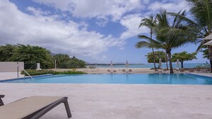 A pool area with lounge chairs and umbrellas, a beach view, and palm trees. - Beachfront Apt - Playa Dorado, Puerto Plata (Puerto Plata,)