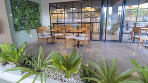 An indoor seating area with wooden tables and chairs, a glass wall with 'ONE ONE ONE ONE' text, and a green wall with plants. - Beachfront Apt - Playa Dorado, Puerto Plata (Puerto Plata,)