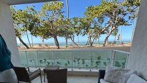 A balcony with wicker furniture, a white sofa, and a view of the beach and ocean. - Beachfront Apt - Playa Dorado, Puerto Plata (Puerto Plata,)