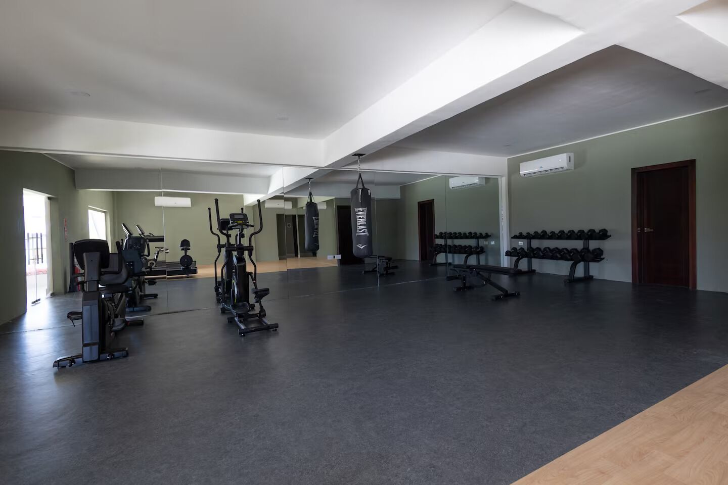 A spacious gym with cardio machines, weightlifting equipment, and dumbbells.
