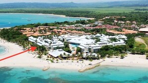 An aerial view of a resort with multiple buildings, a beach, and clear turquoise waters. - Beachfront Apt - Playa Dorado, Puerto Plata (Puerto Plata,)