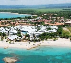 An aerial view of a resort with multiple buildings, a beach, and clear turquoise waters.