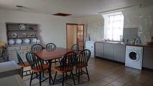 A compact kitchen with a dining area, featuring a wooden table and chairs, a washing machine, and a shelf with decorative plates. - 4-bed Property in Converted Coach House in Turriff (Turriff)