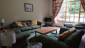 A living room with a sofa set, a coffee table, a television, and a window with curtains. - 4-bed Property in Converted Coach House in Turriff (Turriff)
