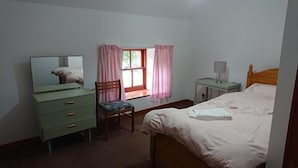 A bedroom with a bed, a dresser, a chair, a nightstand, and a window with curtains. - 4-bed Property in Converted Coach House in Turriff (Turriff)