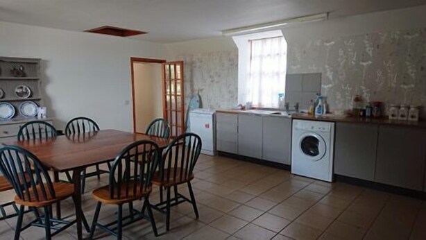 A compact kitchen with a dining area, a washing machine, and a small refrigerator. - 4-bed Property in Converted Coach House in Turriff (Turriff)