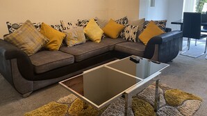 Un salon moderne avec un canapé d’angle, une table basse en verre et un tapis à motifs.