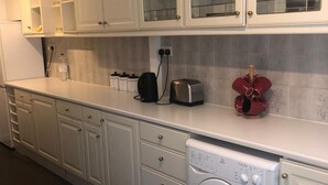 Une cuisine moderne avec des meubles blancs, un lave-linge encastré et un plan de travail sur lequel se trouvent un grille-pain et une bouilloire.