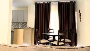 Un coin repas avec une table et des chaises, une cuisine à l’arrière-plan et un rideau qui sépare l’espace.
