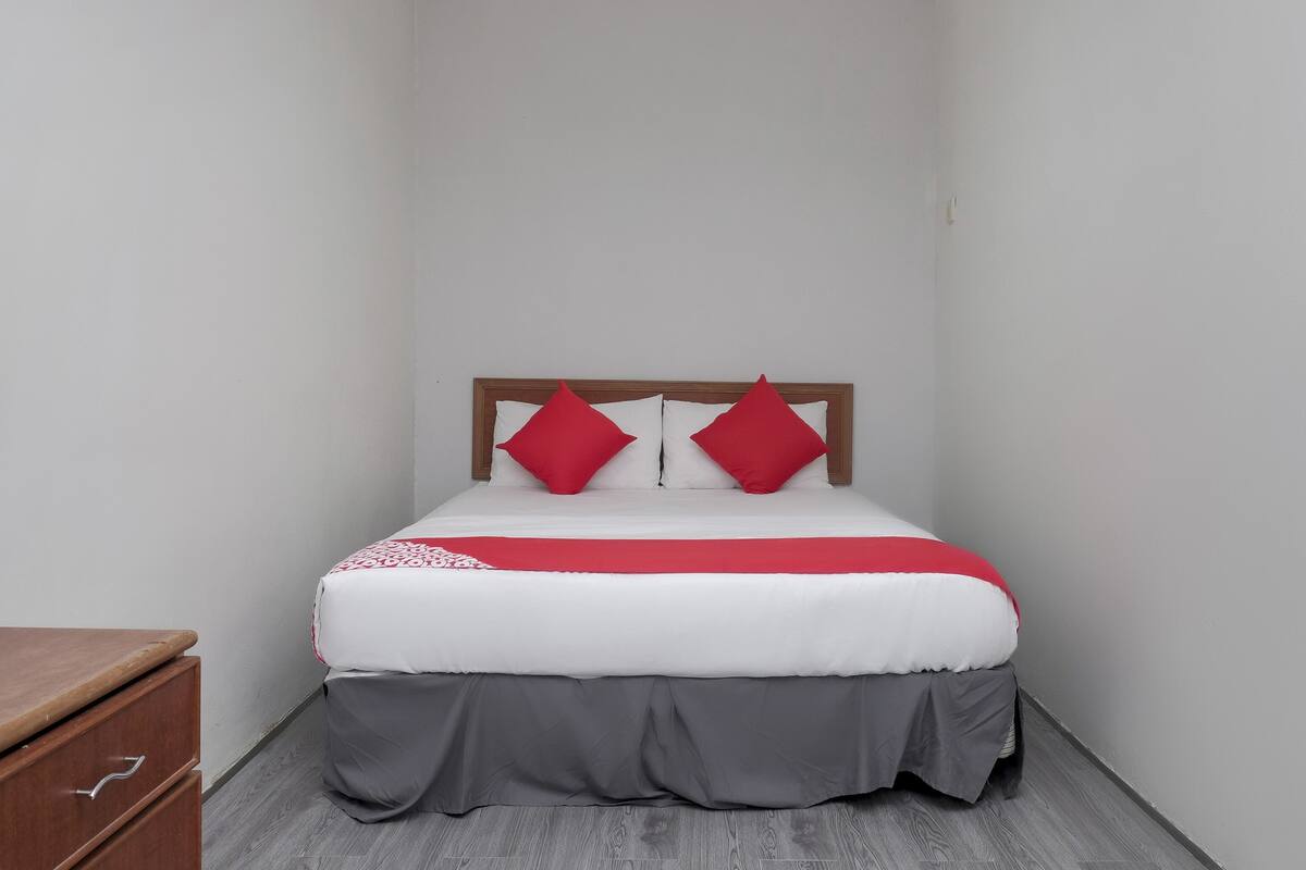 Een kleine, smalle kamer met een enkel bed, een houten hoofdbord en een houten dressoir.