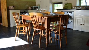 Een eetgedeelte met een houten tafel en stoelen, een keuken met apparatuur, en een raam met natuurlijk licht.