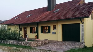 A single-story house with a red-tiled roof, a yellow facade, and a stone-paved entrance.