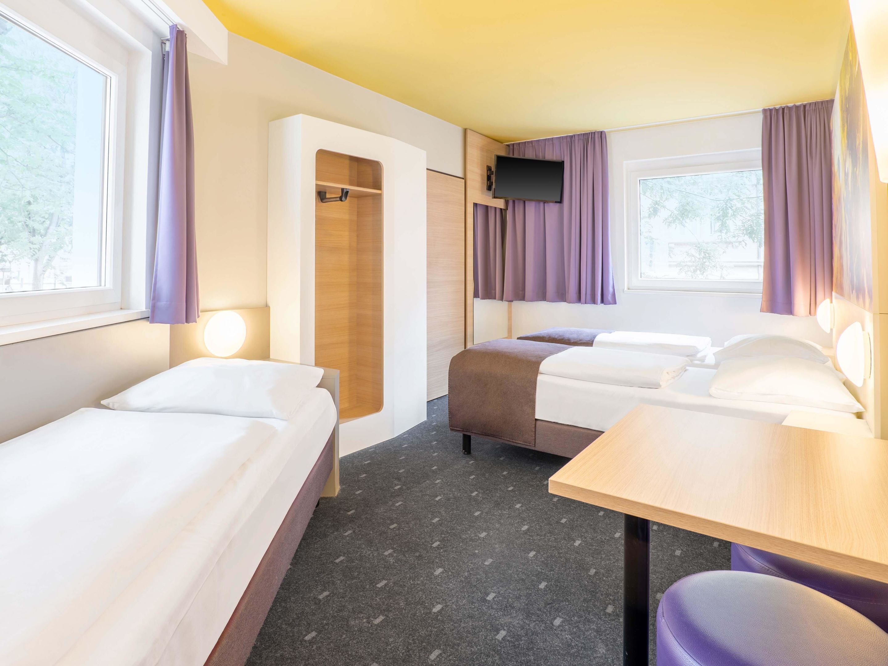 Habitación de hotel con dos camas, un escritorio, un televisor y un armario.