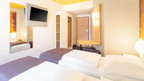 Una habitación de hotel con dos camas, un televisor montado en la pared, un armario de madera y una pequeña mesa.