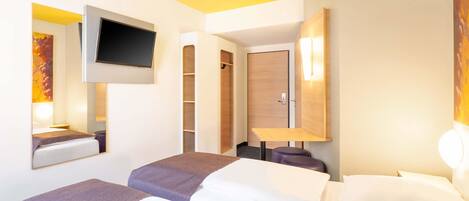 Una habitación de hotel con dos camas, un televisor montado en la pared, un armario de madera y una pequeña mesa.