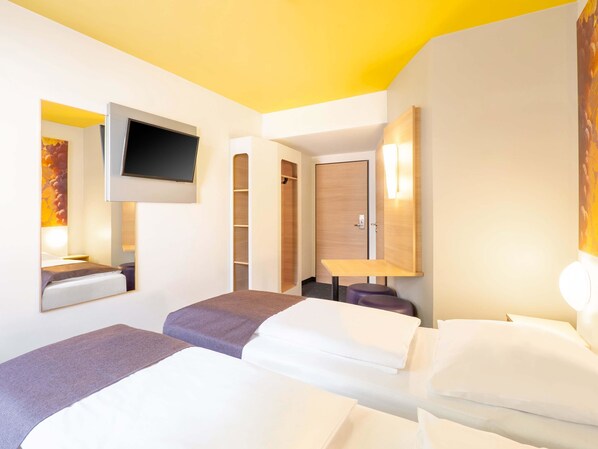 A hotel room with two beds, a TV mounted on the wall, a wooden wardrobe, and a small table. - B&B Hotel Heilbronn (Heilbronn)