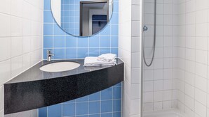 Un baño con lavamanos de encimera negra, un espejo redondo y zona de ducha.