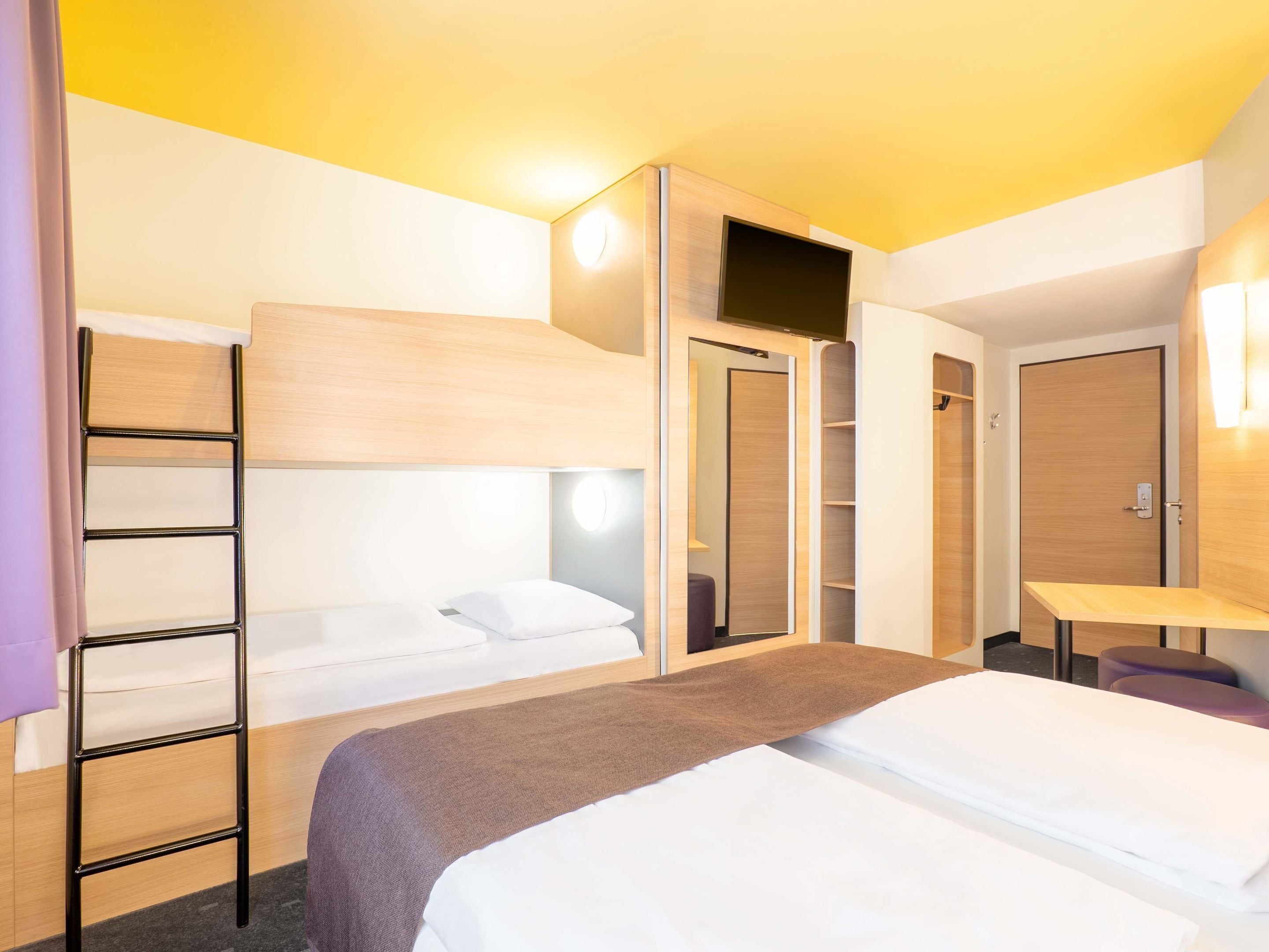 A hotel room with a bunk bed, a desk, a wardrobe, and a bathroom.
