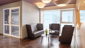 Un área de descanso moderna con un sofá, dos sillones y una mesita con plantas en macetas. Grandes ventanales ofrecen vistas de la ciudad.