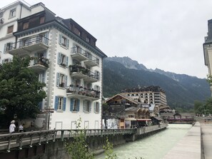 Ein Hotel mit mehreren Balkonen, einem Fluss im Vordergrund und Bergen im Hintergrund.
