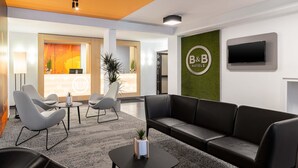 A hotel reception area with a reception desk, seating area, and a television screen. - B&B HOTEL Essen-City (Essen)
