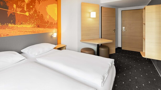 A hotel room with two beds, a desk, a wardrobe, and a large wall mural. - B&B HOTEL Essen-City (Essen)