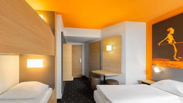 Ein Hotelzimmer mit zwei Betten, einem kleinen Schreibtisch, einem Sessel und einem Nachttisch. Ein Flur führt zu einem anderen Zimmer.