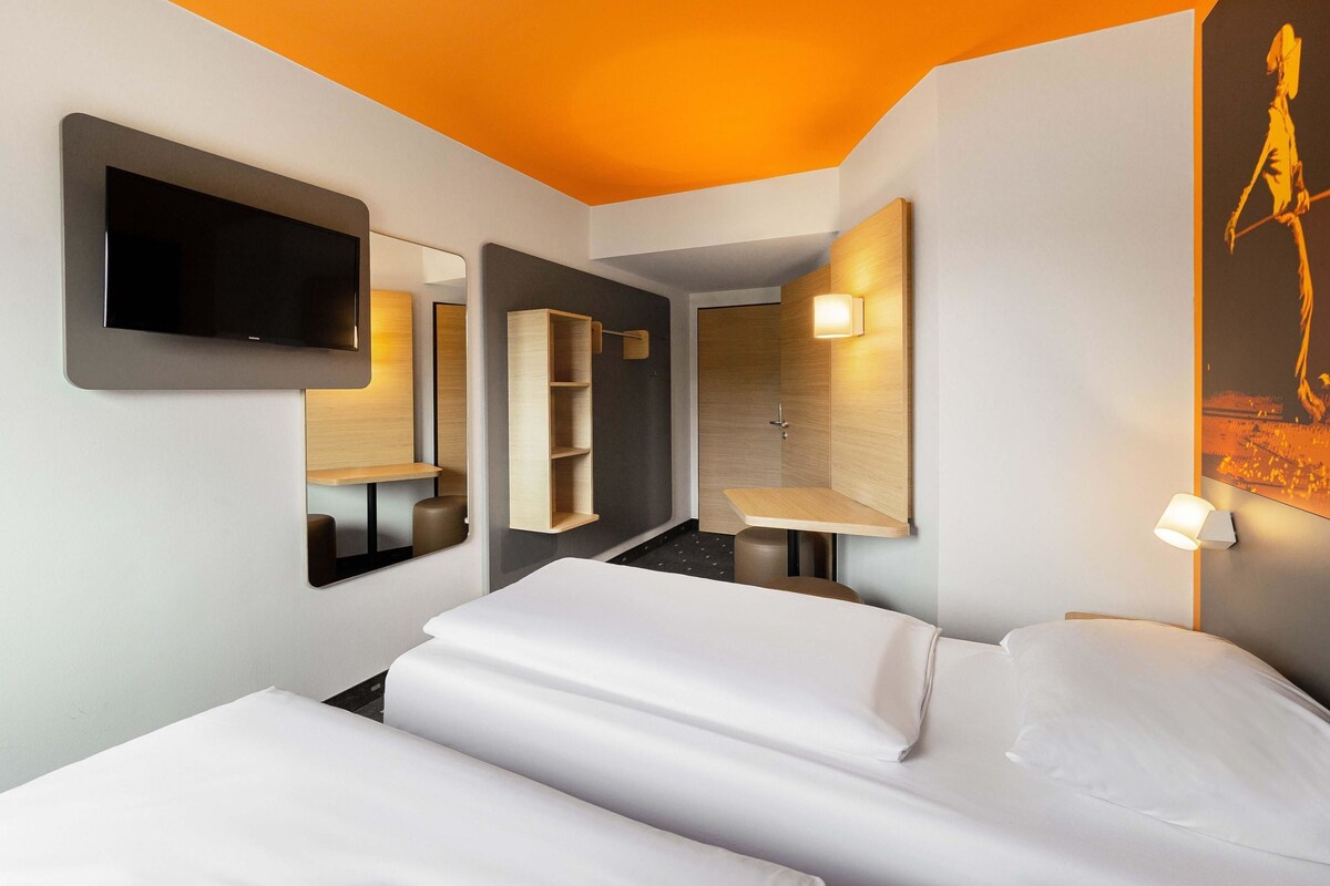 A modern hotel room with a large bed, a TV, a mirror, and a shower area.