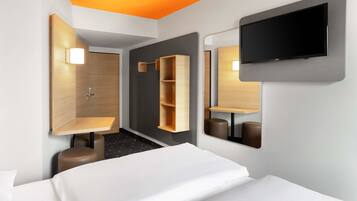 Ein modernes Hotelzimmer mit Bett, Duschbereich und einem an der Wand befestigten Fernseher.