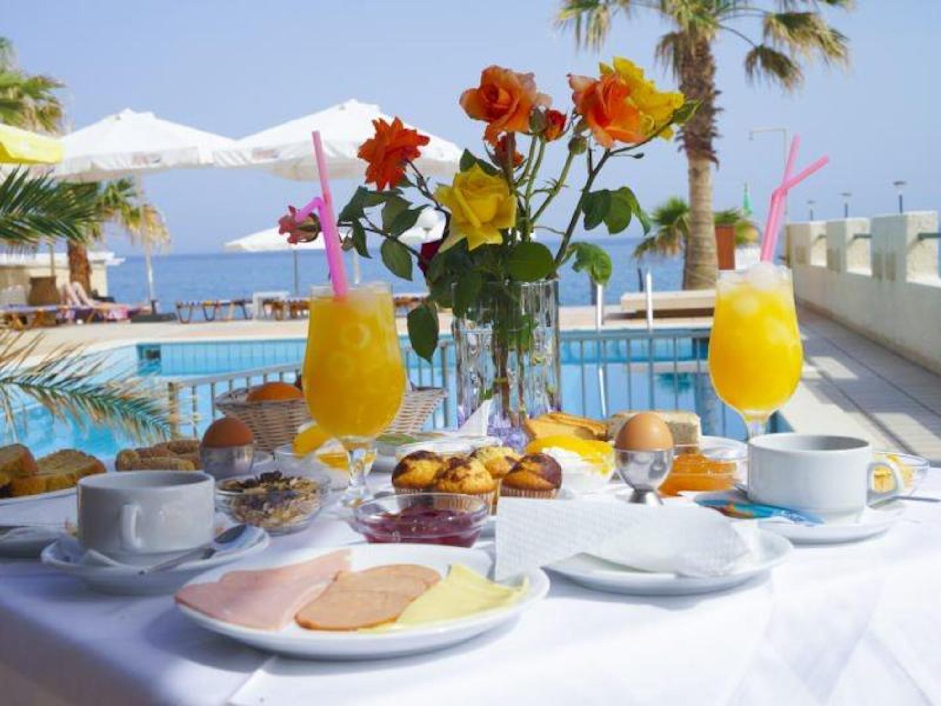 A breakfast setup with a pool view, including plates of food, drinks, and a vase of flowers.
