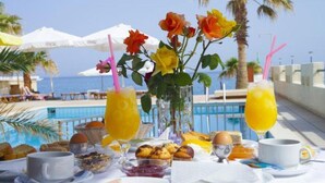 A breakfast setup with a pool view, including plates of food, drinks, and a vase of flowers. - Apartment for 4 Persons, Swimming Pool, Near the Beach (Rethymno)