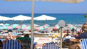 A beachside setting with multiple umbrellas and lounge chairs, a clear view of the ocean, and a tiled floor. - Apartment for 4 Persons, Swimming Pool, Near the Beach (Rethymno)