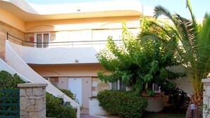 A two-story building with a curved facade, stone walls, and a small garden with palm trees and shrubs. - Apartment for 4 Persons, Swimming Pool, Near the Beach (Rethymno)