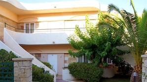 A two-story building with a curved facade, stone walls, and a small garden with palm trees and shrubs. - Apartment for Five, Swimming Pool, Near the Beach (Rethymno)