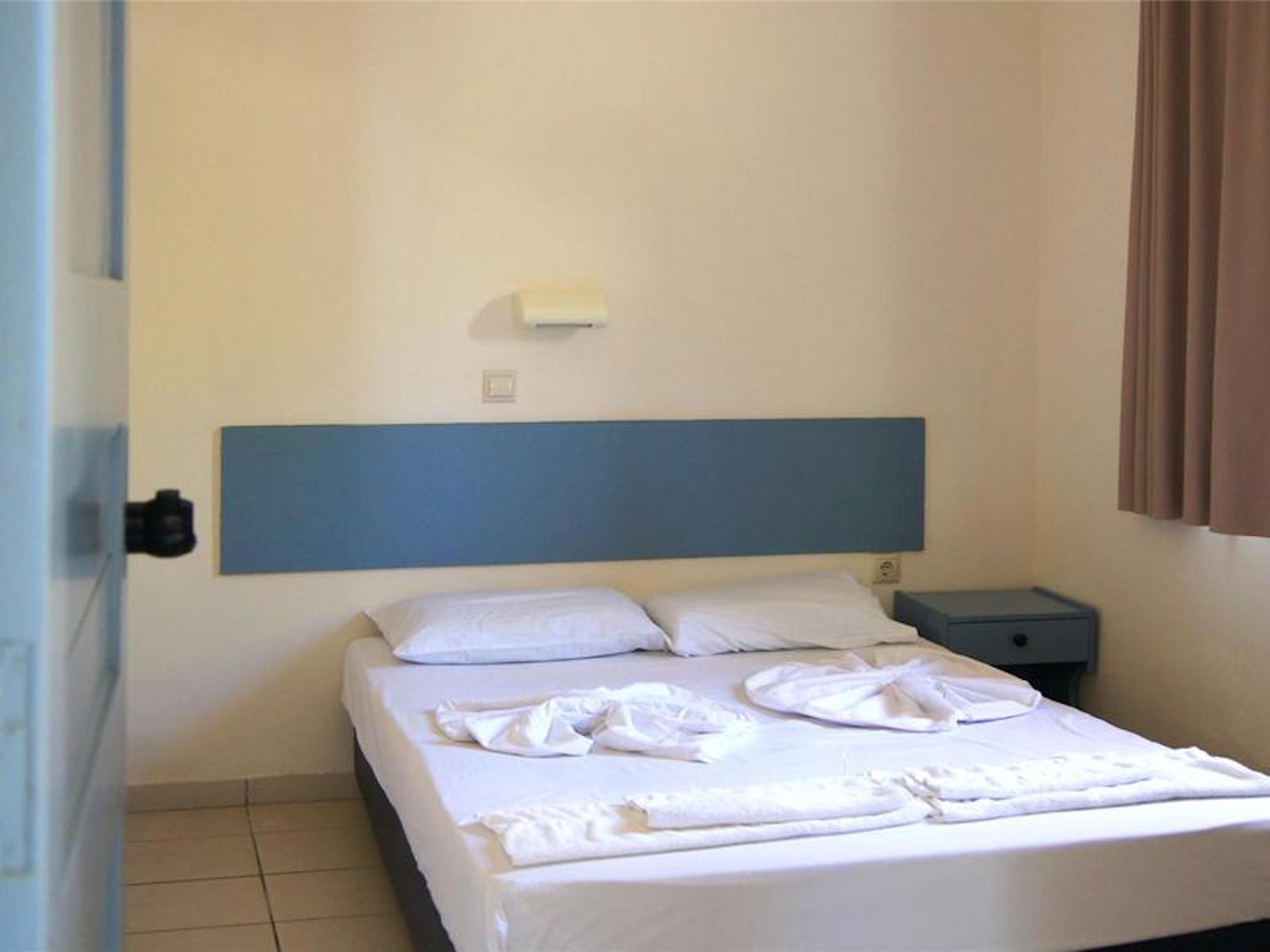 A hotel room with a bed, a nightstand, a wall-mounted light, and a window with curtains.