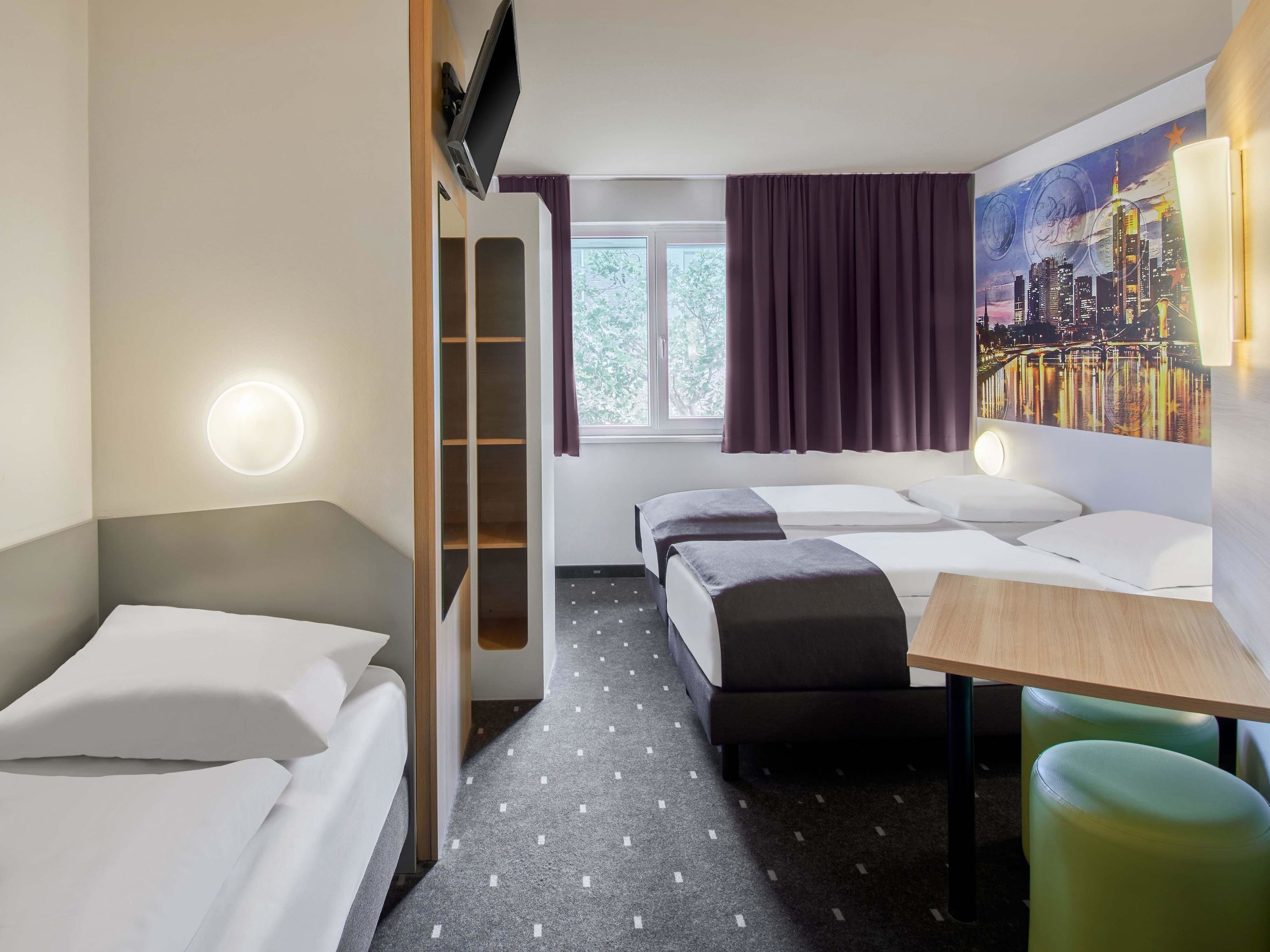 A hotel room with a bed, a desk, a chair, a wardrobe, and a painting on the wall.