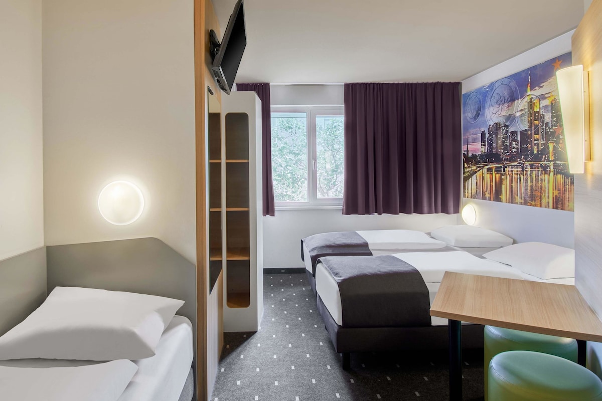 A hotel room with a bed, a desk, a chair, a wardrobe, and a painting on the wall.