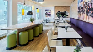 A modern restaurant interior with a bar area, seating, and a cityscape mural. - B&B Hotel Frankfurt City-Ost (Frankfurt)