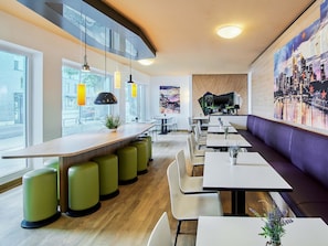 A modern restaurant interior with a bar area, seating, and a cityscape mural. - B&B Hotel Frankfurt City-Ost (Frankfurt)