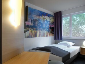 A hotel room with a bed, a desk, a window with curtains, and a cityscape mural on the wall. - B&B Hotel Frankfurt City-Ost (Frankfurt)