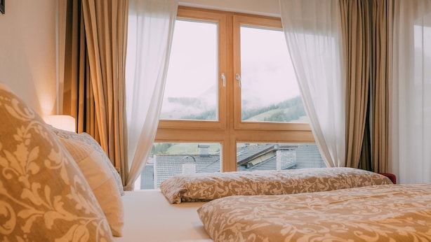 A bedroom with two beds, a window with curtains, and a view of buildings outside. - 1: Three-room Apartment With Panoramic View (Badia)