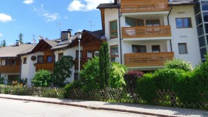A row of residential buildings with balconies, a wooden fence, and lush greenery. - 1: Three-room Apartment With Panoramic View (Badia)