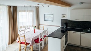 A compact kitchen with white cabinets, a black countertop, and a small island. There is a dining table with chairs and a vase with a red flower. - 1: Three-room Apartment With Panoramic View (Badia)