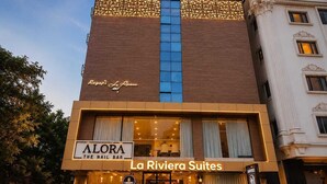 Um hotel com fachada moderna, uma placa para 'ALORA THE NAIL BAR' e 'La Riviera Suites', indicando um estabelecimento de hotel e bar.