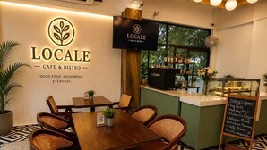 Interior de café com mesa e cadeiras de madeira, um quadro de menu e um balcão com máquina de café.