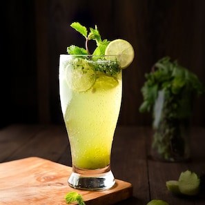 A tall glass with a lime wedge and mint leaves, placed on a wooden surface. - Room-la Riviera Suites Premium Stay in (Hyderabad)