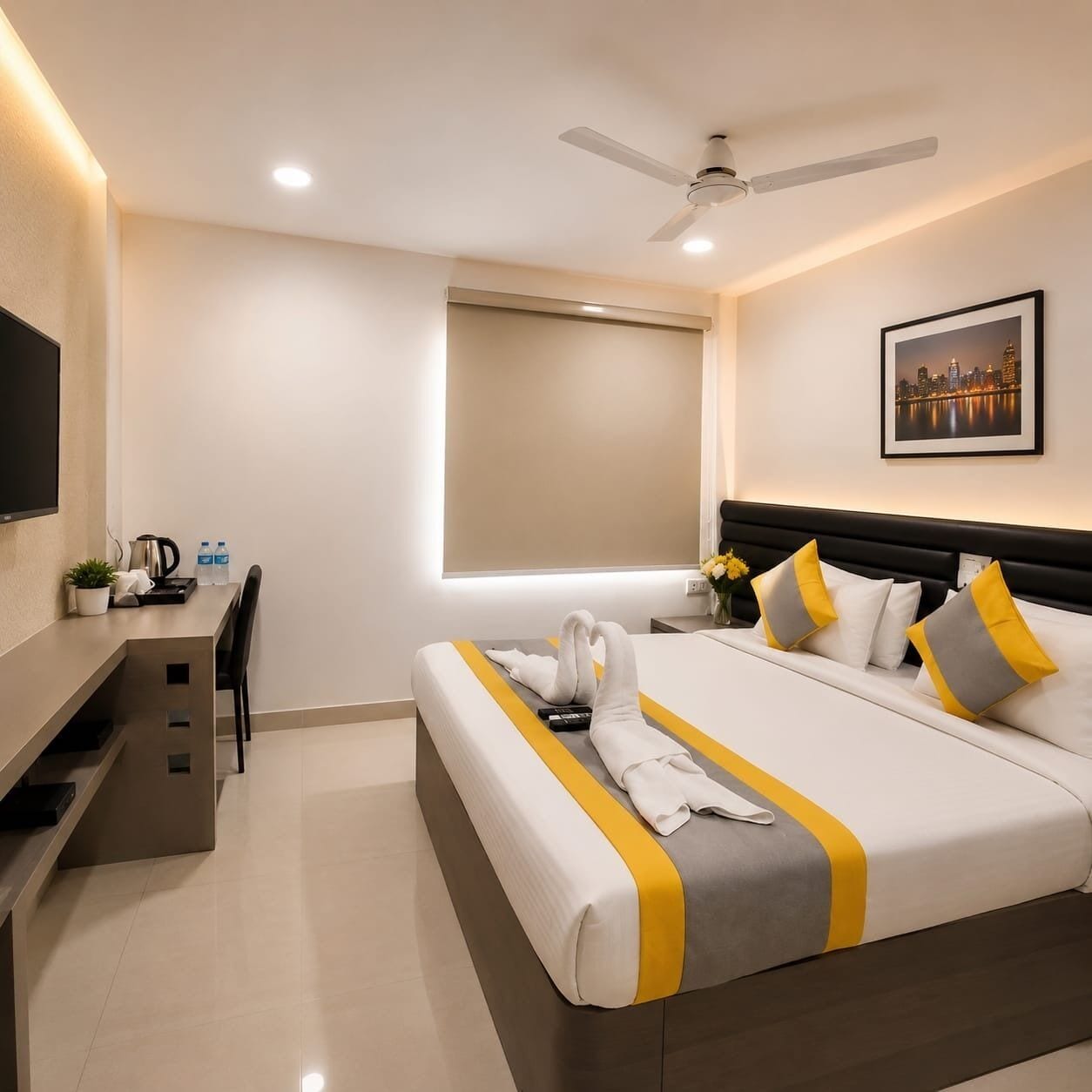 A hotel room with a bed, a desk, a chair, a ceiling fan, a window with a blind, and a framed picture on the wall.