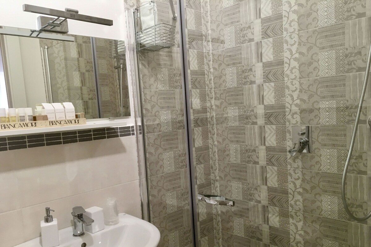 A bathroom with a glass-enclosed shower, a sink with a mirror above it, and patterned tiles on the walls.