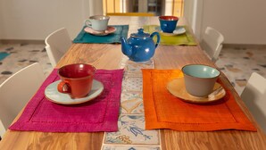 A wooden dining table with colorful placemats and ceramic cups and saucers.