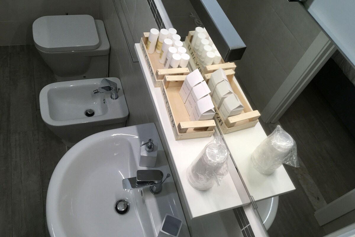 A bathroom with a toilet, bidet, and sink. There are toiletries and a small mirror on the counter.